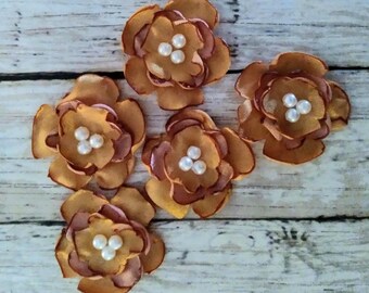 May include: Five brown fabric flowers with white pearl centers. The flowers are layered and have a slightly ruffled texture.