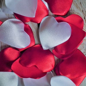 May include: A collection of red and white satin heart-shaped decorations. The hearts are arranged in a random pattern on a wooden surface.