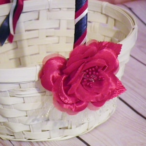May include: White wicker basket with a red fabric flower and a blue and white striped ribbon handle.