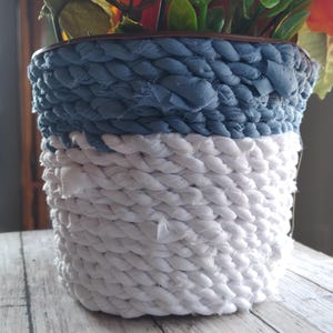 Puede incluir: Un macetero de tela azul y blanco con textura tejida. El macetero está hecho de tela trenzada y tiene un aspecto rústico y hecho a mano.