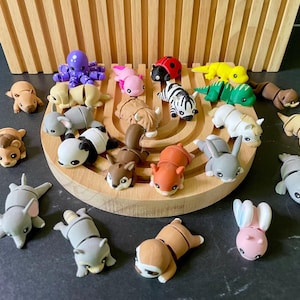 Könnte beinhalten: Eine Sammlung kleiner, beweglicher Tierfiguren in verschiedenen Farben und Arten, darunter ein violetter Oktopus, ein roter Marienkäfer, eine gelbe Eidechse, ein Panda, ein Zebra und ein Faultier, angeordnet auf einem hellen, halbkreisförmigen Holzständer.