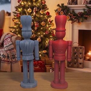 Könnte beinhalten: Zwei stehende Nussknacker-Figuren, eine in mattem Hellblau mit gerippter Textur und eine in einfarbigem Mattrot. Beide Figuren haben hohe zylindrische Hüte, uniformartige Jacken mit Schulterklappen und runde Sockel für einen stabilen Stand.