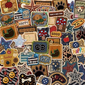 Op de afbeelding: Een verzameling diverse stoffen patches met verschillende ontwerpen, waaronder sterren, dieren, paddenstoelen, smileygezichten en teksten zoals HAPPY, RICH en SHINE LIKE THE STARS, versierd met knopen, stiksels en diverse patronen.