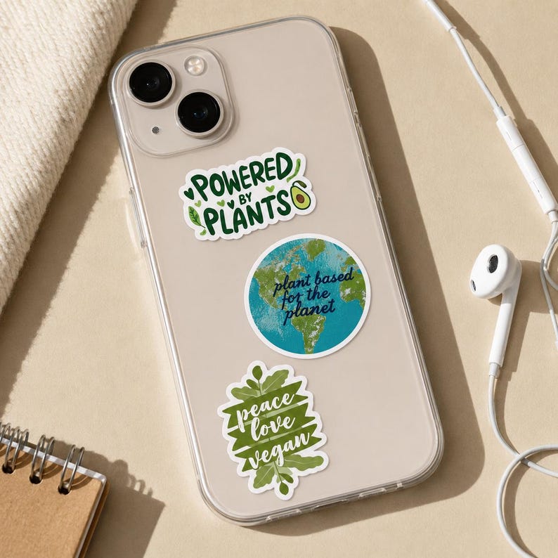 May include: A clear smartphone case decorated with three stickers. The top sticker reads "POWERED BY PLANTS" with an avocado icon. The middle circular sticker shows a globe with the text "plant based for the planet". The bottom sticker says "peace love vegan".