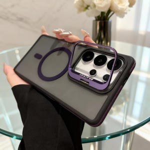 Puede incluir: Una funda de smartphone negro mate con parte trasera translúcida, que presenta un anillo magnético circular de color morado oscuro y una cubierta de lente de cámara metálica a juego que sirve de soporte, con la palabra BRACKET en el marco.