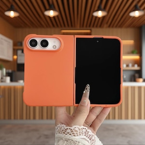 May include: A bright orange foldable smartphone case featuring a smooth matte finish. The case includes a dedicated cutout for a dual-camera system with a flash and a large rectangular opening for the foldable screen display area.