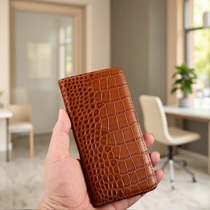 May include: A rectangular brown wallet featuring a textured crocodile skin pattern. The wallet has a vertical orientation with visible stitching along the edges and a smooth, glossy finish across the entire surface of the exterior cover.