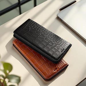 Peut inclure: Deux étuis de téléphone rectangulaires avec un motif texturé en peau de crocodile. Un étui est noir uni et l'autre est marron clair. Les deux étuis présentent un design fin et pliable avec une découpe pour appareil photo sur l'étui marron.