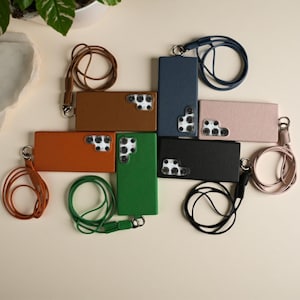May include: A collection of seven rectangular smartphone cases with textured surfaces in brown, orange, green, dark blue, light pink, and black. Each case features a cutout for a multi-lens camera system and includes a matching detachable lanyard.