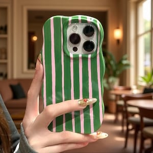 Peut inclure: Une coque de smartphone aux bords ondulés présentant un motif à rayures verticales vert foncé et rose clair. La coque possède un rebord moulé et surélevé autour de l'ouverture de l'appareil photo, révélant trois objectifs et un flash.