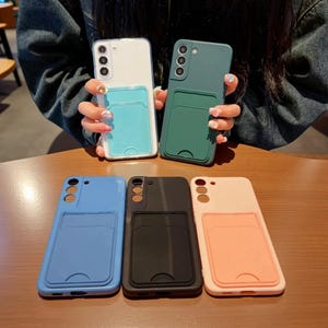 Puede incluir: Una colección de cinco fundas para smartphone con ranuras para tarjetas integradas en la parte posterior. Las fundas vienen en blanco con ranura azul claro, verde oscuro, azul, negro y melocotón, cada una con recorte para triple cámara.