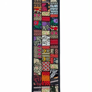 Peut inclure: Un chemin de table rectangulaire composé d'un assemblage de carrés de tissu brodés aux couleurs vives, notamment rouge, jaune, vert, violet et noir. Le chemin de table est bordé de tissu noir et terminé par des pompons noirs à chaque coin.