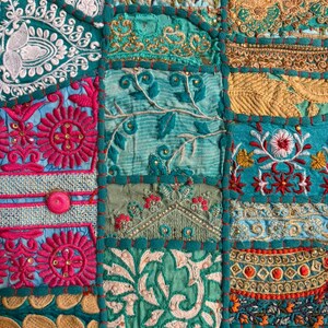 Pode incluir: Um t&ecirc;xtil de patchwork com uma gama vibrante de pain&eacute;is de tecido em tons de azul-petr&oacute;leo, magenta e dourado. A superf&iacute;cie &eacute; densamente decorada com bordados intrincados, fios met&aacute;licos, lantejoulas e padr&otilde;es florais em relevo, unidos por costuras grossas em azul-petr&oacute;leo.