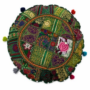 May include: A round floor cushion featuring a patchwork design of green, purple, and gold fabric panels with intricate embroidery, metallic thread detailing, and floral motifs. The edges are finished with small white beads and colorful tassels.