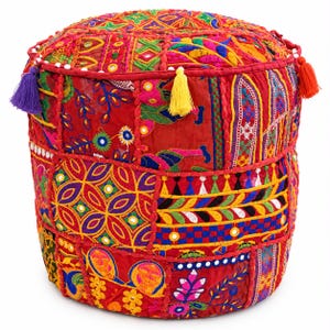 May include: A cylindrical floor pouf featuring a vibrant patchwork of red fabric panels adorned with intricate multi-coloured embroidery, small circular mirrors, and decorative stitching. The top and sides are accented with colourful tassels.