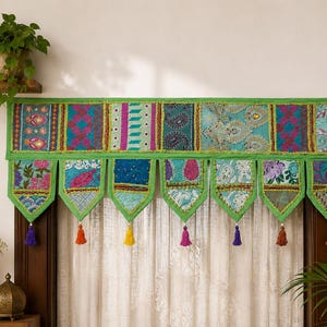 Op de afbeelding: Een rechthoekige raamvalance met een patchwork van levendige, veelkleurige stoffen panelen in tinten groen, blauwgroen, roze en blauw. De onderrand heeft zeven puntige tabs, elk afgewerkt met een kleine, bungelende kleurrijke kwast.