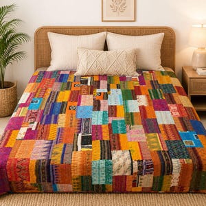 Puede incluir: Una colcha rectangular con un diseño de patchwork compuesto por numerosos rectángulos de tela pequeños y multicolores en tonos naranja, amarillo, azul, verde y morado, con detalles de costura visibles en toda la superficie.