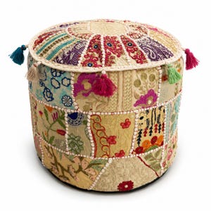May include: A round, cylindrical ottoman featuring a patchwork design of various embroidered fabrics in shades of cream, gold, pink, blue, and purple. The surface is decorated with floral patterns, sequins, and small tassels in teal, beige, pink, and green.