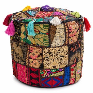 May include: A cylindrical ottoman featuring a patchwork design of various embroidered fabrics in black, gold, red, blue, and pink. The surface is adorned with intricate floral and geometric patterns, accented by multiple colorful tassels along the top edge.