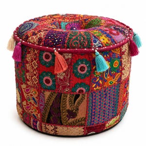Puede incluir: Un puf cilíndrico redondo con un diseño de retazos de varias telas rojas, doradas, verdes y azules. La superficie está decorada con intrincados bordados, patrones florales y motivos de cachemira, terminada con borlas colgantes de colores.