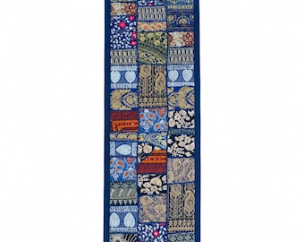 Pode incluir: Um caminho de mesa retangular com um design de patchwork de vários quadrados de tecido bordados em azul, dourado e branco. O caminho é contornado com tecido azul escuro sólido e finalizado com pequenas borlas azul escuro nos quatro cantos.