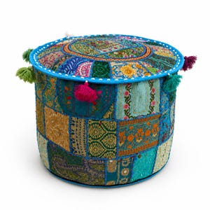 May include: A round ottoman featuring a patchwork design of various fabrics in shades of blue, green, gold, and pink. The surface is adorned with intricate embroidery, beadwork, and sequins, finished with a bright blue trim and colorful tassels.