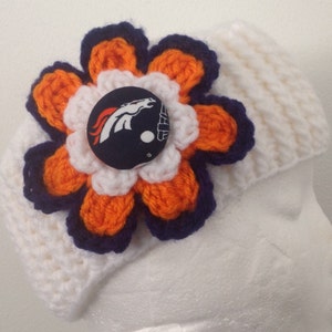 May include: White crocheted headband with a large orange, white, and navy blue crocheted flower. The center of the flower has a fabric button with a football helmet and horse logo.