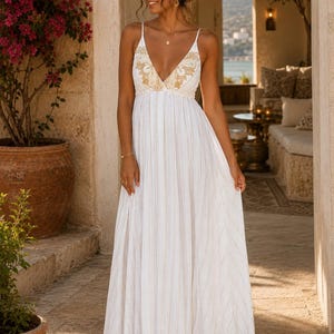 Könnte beinhalten: Ein bodenlanges weißes Maxikleid mit dünnen Spaghettiträgern, einem tiefen V-Ausschnitt und goldener Blumenstickerei am Oberteil. Der Rock besteht aus leichtem, plissiertem Stoff mit dezenten vertikalen goldenen Metallic-Nadelstreifen.