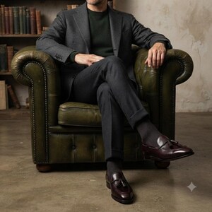 May include: A charcoal gray wool blazer and matching trousers worn over a dark green sweater. The outfit is paired with dark gray ribbed socks and polished burgundy leather tassel loafers, creating a coordinated ensemble with a classic aesthetic.