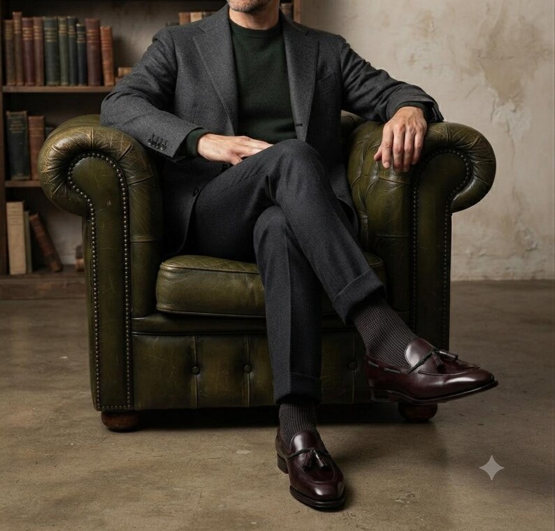 May include: A charcoal gray wool blazer and matching trousers worn over a dark green sweater. The outfit is paired with dark gray ribbed socks and polished burgundy leather tassel loafers, creating a coordinated ensemble with a classic aesthetic.