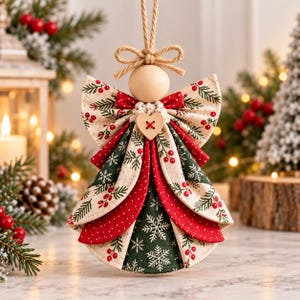 May include: A hanging Christmas ornament shaped like an angel, featuring a smooth wooden bead head, a jute twine bow, and a layered fabric dress. The dress displays patterns of green pine branches, red berries, and white snowflakes on cream, green, and red fabric.