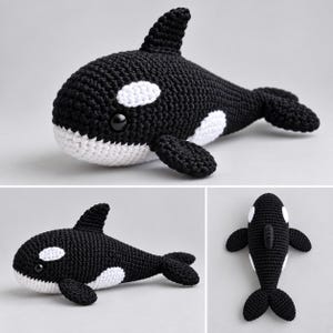 May include: A black and white crocheted orca toy featuring a rounded body, a dorsal fin, side flippers, and a tail fluke. The orca has a white patch near each eye and a white underside, with large, smooth, black plastic eyes set into the head.