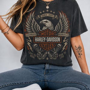 Op de afbeelding: Een antracietgrijs t-shirt met korte mouwen en een afbeelding van een Amerikaanse zeearend met gespreide vleugels boven een Harley-Davidson Motor Cycles logo. De tekst luidt SINCE 1903, LEGENDARY MOTORCYCLES, LIVE TO RIDE en RIDE TO LIVE met bliksemschichten.