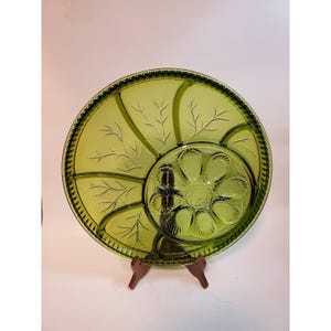 May include: A round, olive green glass serving platter featuring a divided design. The outer section has four segments with embossed leaf patterns, while the central circular section contains a moulded flower shape with eight petals.