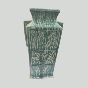 Könnte beinhalten: Eine rechteckige Keramikvase mit glänzender grüner Glasur und einem ausgestellten Rand. Die Oberfläche zeigt geformte Reliefpaneele mit botanischen Motiven wie Blättern und Stängeln sowie einen dunkelgrünen Tropfeffekt auf hellgrünem Grund.