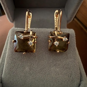 May include: A pair of gold-toned earrings featuring square-cut, translucent brown stones. Each earring is accented with a small gold cross overlay and two tiny, clear, round-cut stones. The earrings have hinged lever-back closures.
