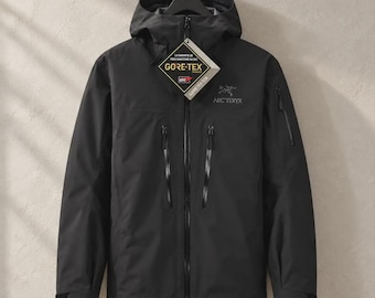 May include: A black Arc'teryx hooded jacket featuring a full-length front zipper, two vertical chest pockets with sealed zippers, and a small zippered pocket on the left sleeve. A diamond-shaped Gore-Tex tag hangs from the main zipper pull.