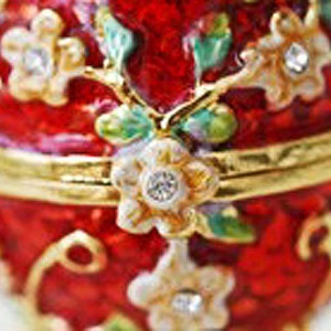 May include: A red, ornate trinket box with gold accents and floral embellishments. The box features a hinged lid and is adorned with white and gold flowers with crystal centers. Green and purple leaves accent the flowers.