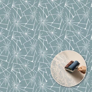 Puede incluir: Un patrón de papel tapiz azul con líneas geométricas blancas y formas de estrella. Un recuadro circular muestra un rodillo de pintura con relieve aplicando un diseño de helecho azul claro sobre una superficie lisa con mango metálico.