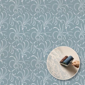 Op de afbeelding: Een patroon van witte, wervelende botanische lijnen op een stoffig blauwe achtergrond. Een cirkelvormig inzetstuk toont een getextureerde verfroller die een lichtblauw varen- en bessenontwerp op een effen oppervlak aanbrengt.