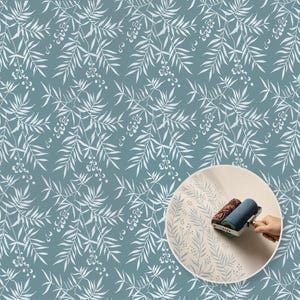 May include: A repeating pattern of white willow branches and small berries on a muted blue background, with an inset circular image showing a patterned paint roller applying the same botanical design onto a light-coloured surface.