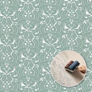 Op de afbeelding: Een saliegroen behang met een herhalend wit damastpatroon met gestileerde bloemmotieven. Een cirkelvormige inzet toont een blauwe patroonverfroller die een delicaat varenachtig ontwerp aanbrengt op een lichtgekleurd oppervlak.