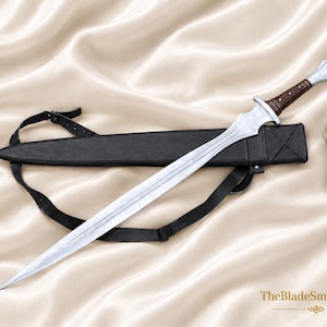 May include: A silver-toned metal sword with a double-edged blade and a brown wrapped handle. The sword features a metallic pommel and crossguard. It is accompanied by a black leather scabbard with an adjustable strap. The text TheBladeSmithCrafts is visible.