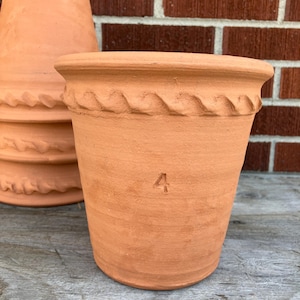 May include: Terracotta flower pot with a decorative wave pattern around the rim. The pot has the number "4" stamped on the side. Other terracotta pots are stacked in the background.