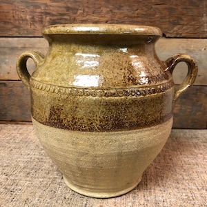 May include: A brown and tan glazed ceramic jar with two handles. The jar has a band of brown glaze around the middle.