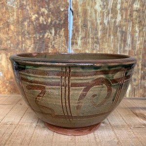 May include: A brown ceramic bowl with a green glaze and brown and white painted designs. The bowl has a rounded shape and a wide rim.