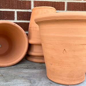 May include: Several terracotta flower pots of varying sizes are arranged against a brick wall. The pots are a warm, earthy orange-brown color. One pot is on its side, revealing its interior. The other pots are upright, showcasing their rims and shapes.