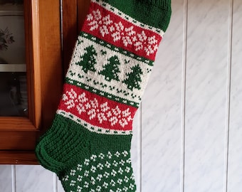 May include: A green, red, and white knitted Christmas stocking with a loop for hanging. The stocking features a pattern of snowflakes and Christmas trees. The toe and heel are green, and the cuff is green.