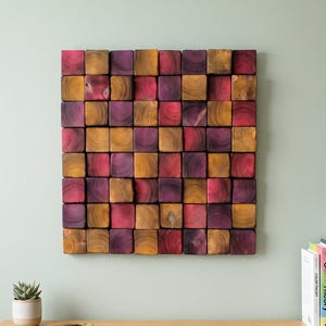 May include: A square wall art piece composed of a grid of individual wooden blocks. Each block features a visible circular wood grain pattern and is stained in alternating shades of deep purple, vibrant magenta, and warm golden yellow.