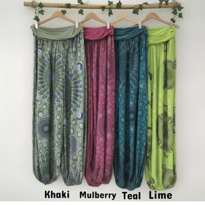 May include: Four pairs of loose-fitting harem trousers hanging on wooden hangers. The trousers feature a fold-over waistband and intricate mandala patterns in khaki, mulberry, teal, and lime green. Each pair has elasticated cuffs at the ankles.
